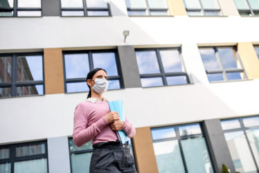 Una docente con mascarilla frente a una institución educativa